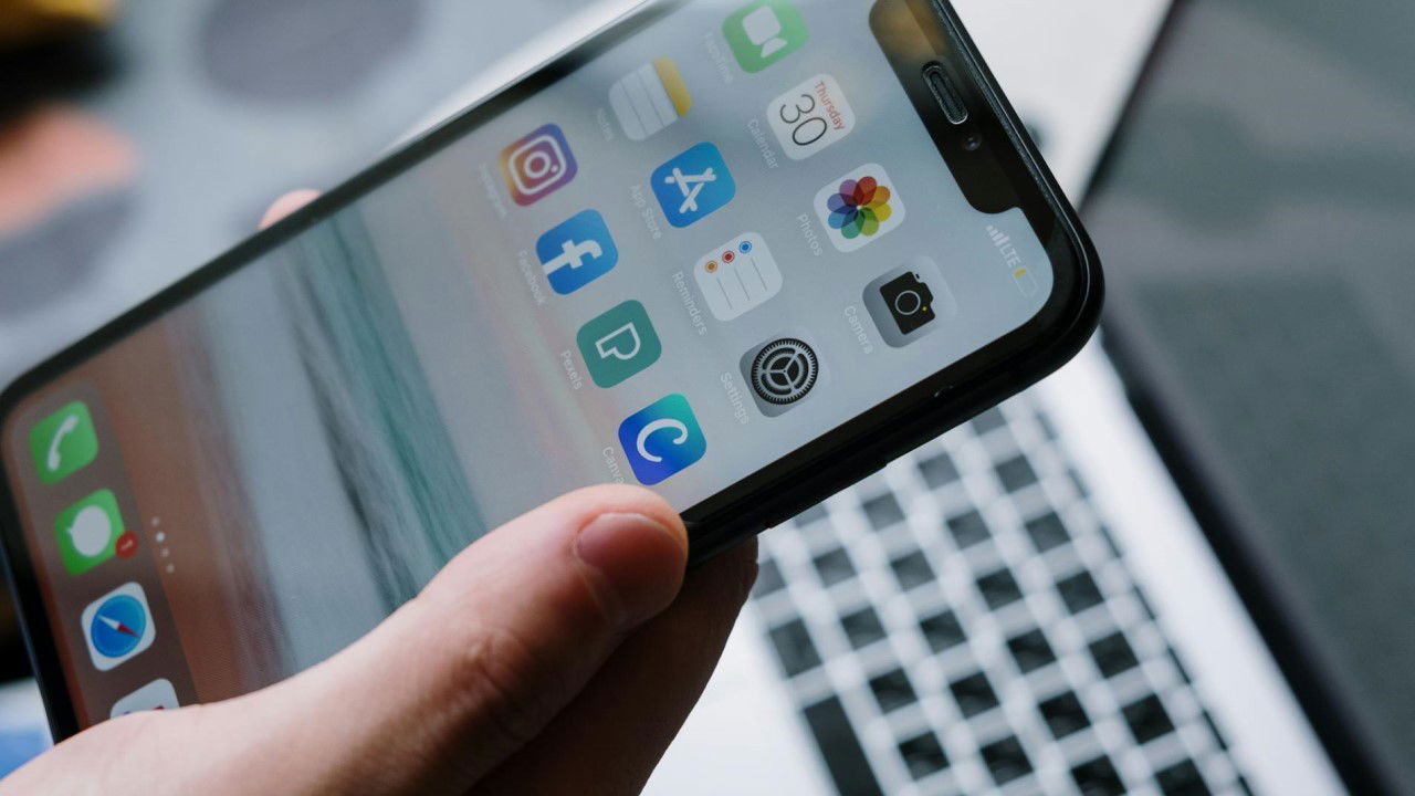 An image of a hand holding a smartphone in front of an open laptop.