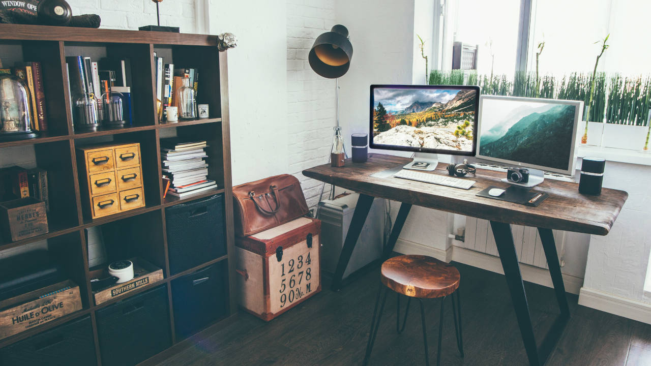 A photograph of a home office setup with two monitors on top of a desk.